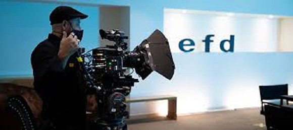 A person in a black cap and shirt operates a large professional film camera in a studio.