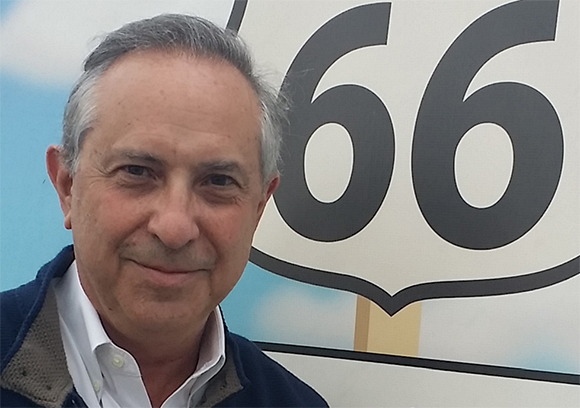 A man with graying hair smiling in front of a large graphic featuring the number 66.