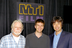 Three men smiling and posing together in front of a black curtain with an MTI Film logo.