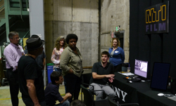 A group of people standing and sitting around a technician at a Sony film equipment booth.