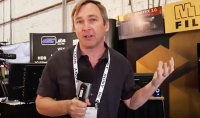 A man in a black shirt holds a microphone and gestures with his hand while speaking.