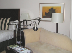 A professional microphone on a stand in front of a beige sofa and a bed in a hotel room.