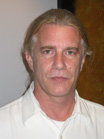A man with long blonde hair and a white collared shirt looking forward.