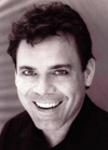 A smiling man with dark, wavy hair looking toward the camera in a black and white portrait.