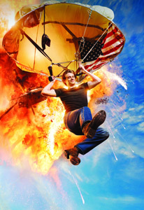 A man in a black shirt and blue jeans falls through the air attached to a parachute featuring the US flag.
