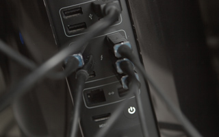 Multiple black cables plugged into the various ports on the back of a black computer tower.
