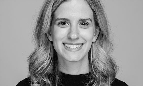 Black and white headshot of a smiling woman with wavy hair against a plain background.