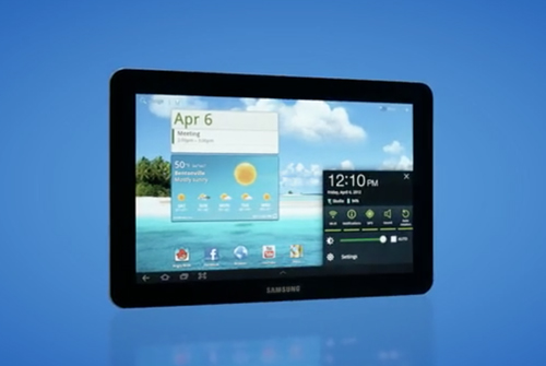 A black Samsung tablet showing a bright blue sky wallpaper with weather, calendar, and clock widgets.