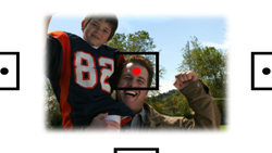 A man laughs while holding a young boy wearing a number 82 football jersey against a backdrop of trees.