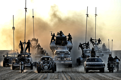 A fleet of post-apocalyptic vehicles and motorcycles driving through thick dust at sunset.