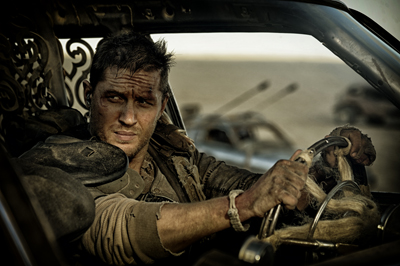 A man with dirt on his face grips a steering wheel while driving through a dusty desert landscape.