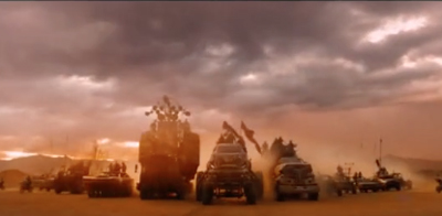 Modified combat vehicles driving through a dusty desert landscape under a dark, cloudy sky.