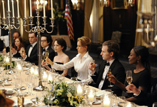 People in formal wear seated at a long table with candles and wine glasses during a dinner event.