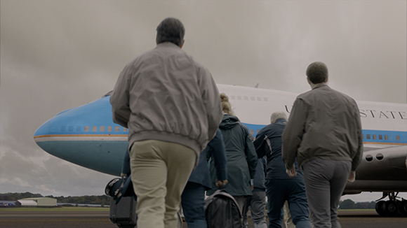 A group of people walking toward a large white and blue airplane under a cloudy sky.