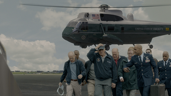 A group of people walking across a tarmac in front of a large dark green United States of America helicopter.