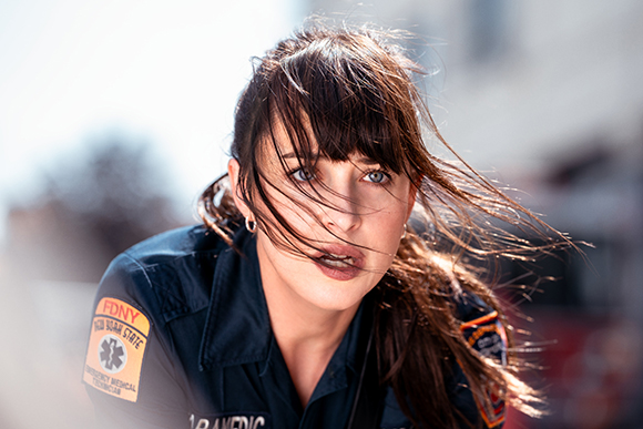 A woman with long brown hair wearing a dark blue FDNY paramedic uniform.