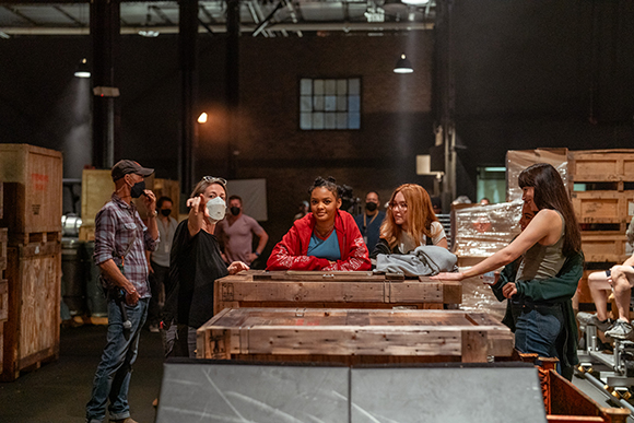 A group of people stand around large wooden crates in a dimly lit warehouse.
