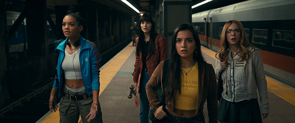 Four young women stand on a dimly lit subway platform looking toward something off-camera with concerned expressions.
