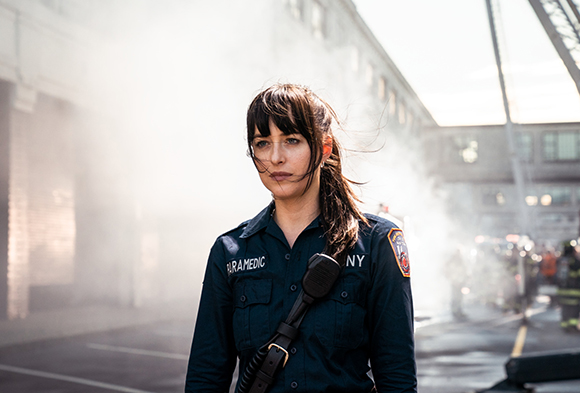 A woman in a dark blue paramedic uniform stands outdoors amidst thick white smoke.