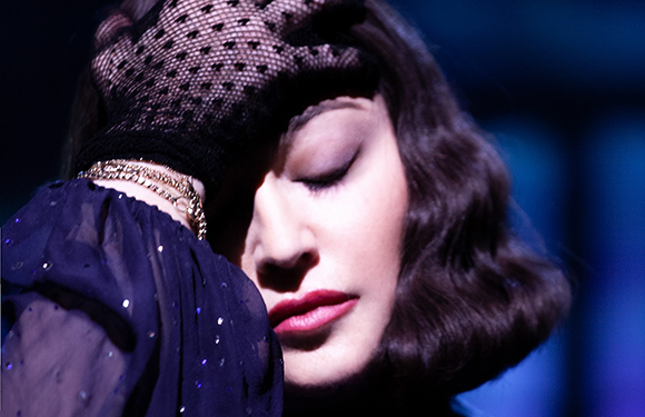 A woman with dark wavy hair rests her face against a black polka-dot mesh glove.