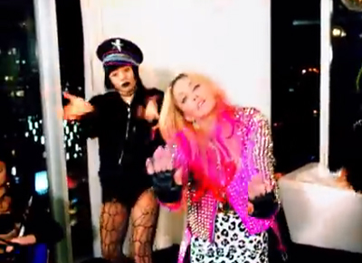 Two women in expressive poses; one in a black hat and outfit, the other in a pink sequined jacket.