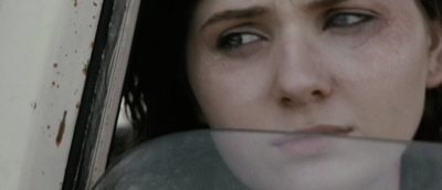 Close-up of a woman with dark hair looking sideways through a car window.