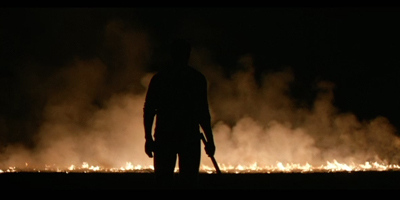 Silhouette of a person standing in front of a line of fire and thick smoke at night.