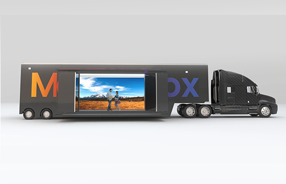 A black semi-truck with a large rectangular digital screen on the side of its trailer displaying a landscape.