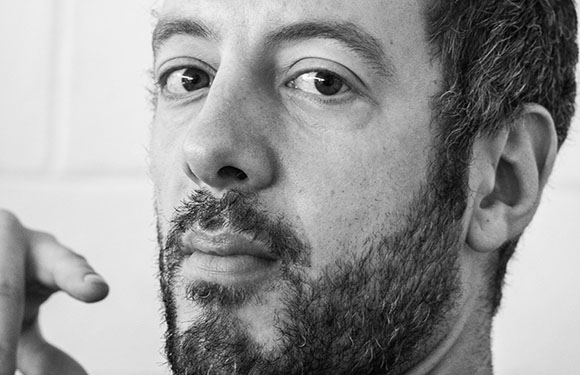 A black and white close-up portrait of a man with short hair and a beard looking toward the camera.