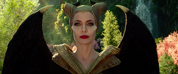 A woman with large black wings, horns, and red lips looking directly at the camera in a forest.