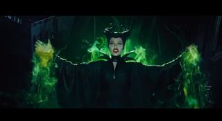 A woman in a black gown and horns stands with arms outstretched amidst swirling green smoke.