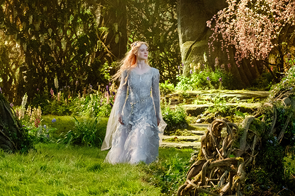 A woman in a long, light blue gown walks through a lush, sunlit forest filled with flowers and ancient trees.