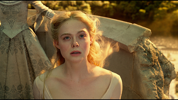 A young blonde woman in a light-colored dress looks ahead with a worried expression outdoors.