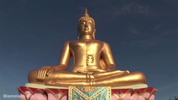 A large golden Buddha statue sitting in a meditative pose on a pink lotus base against a clear blue sky.