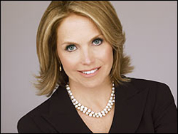 A smiling woman with blonde hair wearing a black blazer and a pearl necklace.