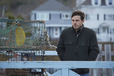 A man in a dark jacket stands outdoors near stacked fishing traps with a house in the background.