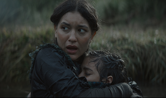 A woman with dark hair looks off to the side with a worried expression while embracing a child.
