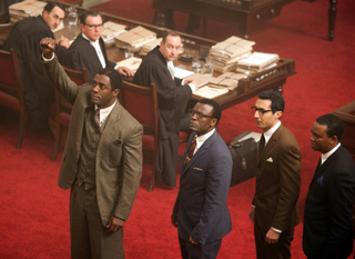 Four men in formal suits standing in a room with red carpeting and wooden furniture.