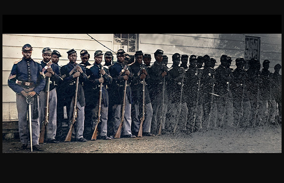A line of Black soldiers in dark blue uniforms and kepis standing in formation with rifles.
