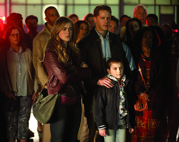A diverse group of adults and a young boy standing together, looking forward with serious expressions.
