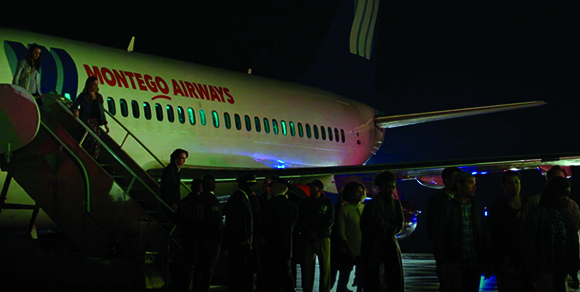 People boarding a Montego Airways airplane via stairs under night lighting.