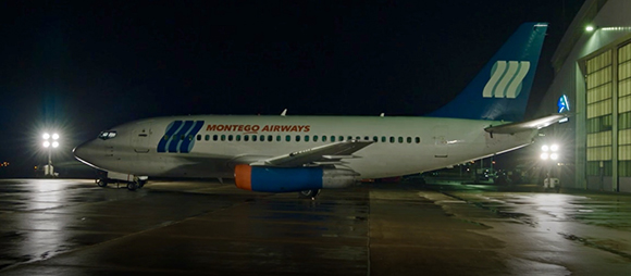 A Montego Airways passenger plane parked on a wet airport tarmac at night next to a hangar.