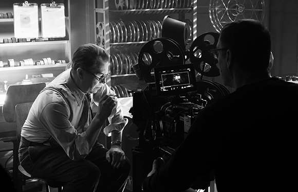 Black and white photo of a man in glasses sitting near a professional film camera and reels.