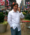A man in a white button-down shirt and jeans talking on a mobile phone in a busy city square.