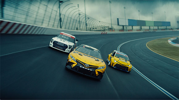 Two yellow Toyota race cars speeding around a curved asphalt track.