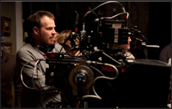 A man wearing headphones operates a large professional cinema camera on a film set.