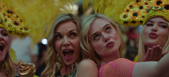 Three women in yellow feathered headpieces pose for a selfie, one blowing a kiss and one with an open mouth.