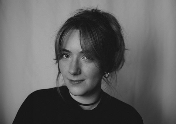 Black and white portrait of a person with light-colored hair, bangs, and a nose ring looking at the camera.