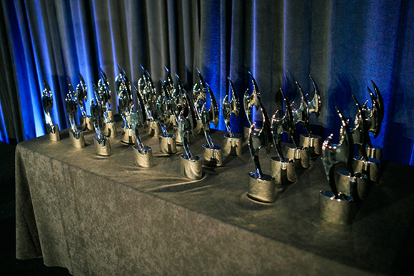 Multiple silver, flame-shaped trophies arranged on a dark cloth-covered table against blue curtains.