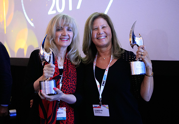 Two women smiling and holding silver crescent-shaped awards at an event.